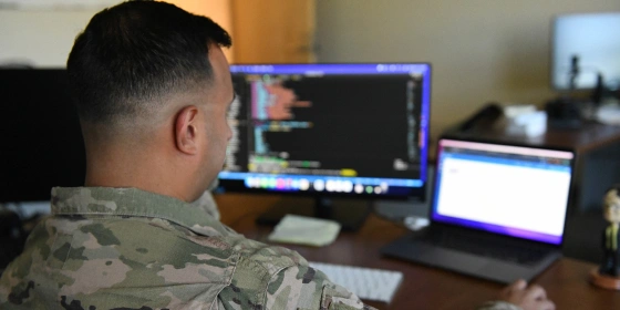 U.S. Airman writing code on a dual-monitor desktop computer.