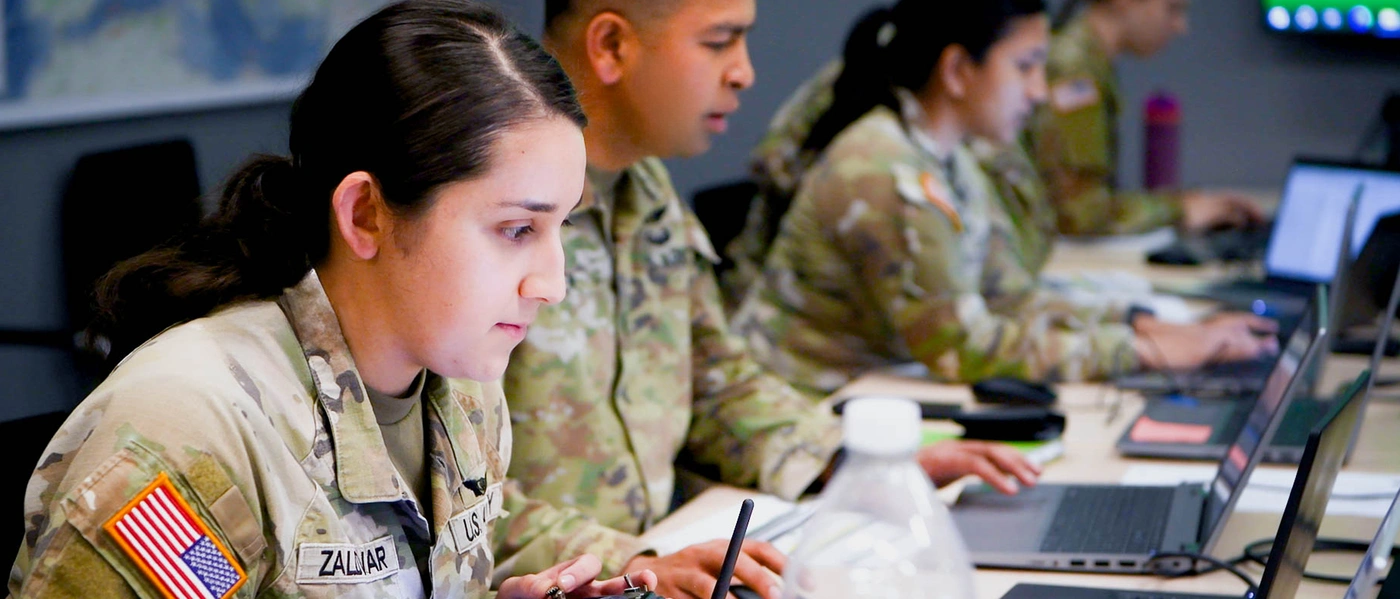 U.S. Army soldiers working on laptops in a classroom setting.