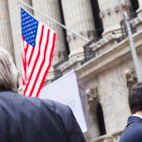 Two men in suits outside a government building with American flags.