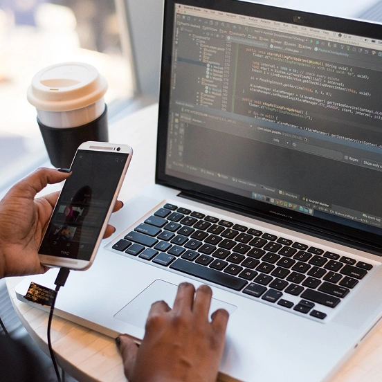 Person coding on a laptop while holding a smartphone.