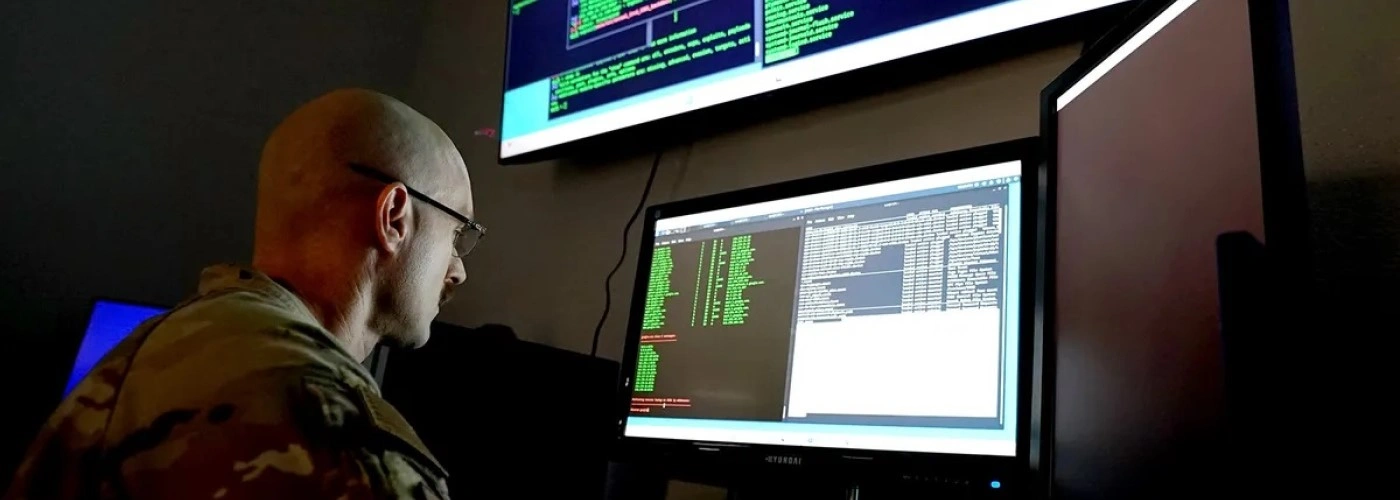 A uniformed researcher works at a computer 1400x500