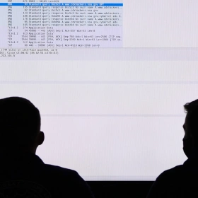 Two US Coast Guard personnel participate in a cybersecurity exercise in front of a large monitor.