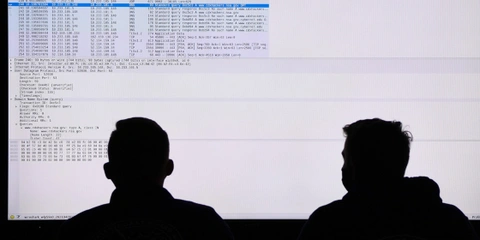 Two US Coast Guard personnel participate in a cybersecurity exercise in front of a large monitor.