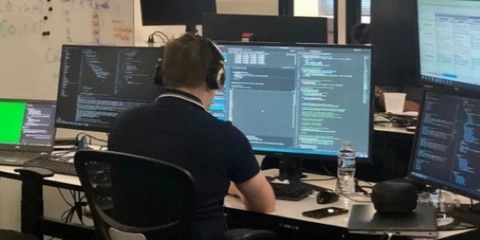 US Air Force developer surrounded by computer monitors working in an office.