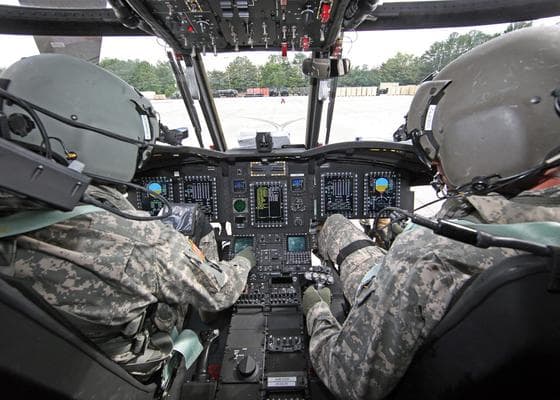 Two military personnel in the front of a helicopter.